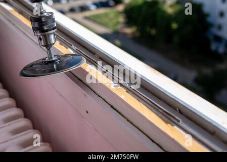 Levigare un vecchio telaio della finestra durante i lavori di ristrutturazione con un parco di un quartiere residenziale della città in uno sfondo Foto Stock