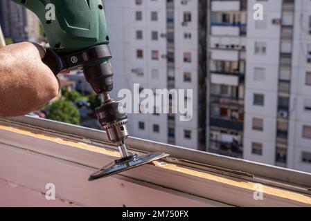 Levigare un vecchio telaio della finestra durante i lavori di ristrutturazione con un edificio di appartamenti sullo sfondo Foto Stock