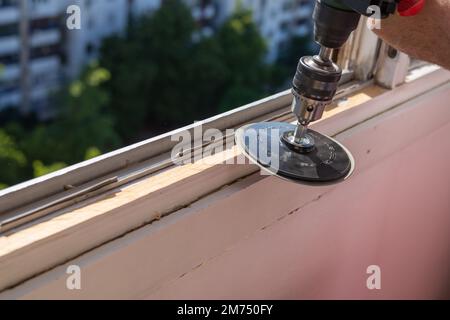 Levigare un vecchio telaio della finestra durante i lavori di ristrutturazione con un edificio di appartamenti sullo sfondo Foto Stock