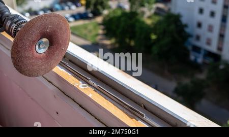 Levigare un vecchio telaio della finestra durante i lavori di ristrutturazione con un parco di un quartiere residenziale della città in uno sfondo Foto Stock