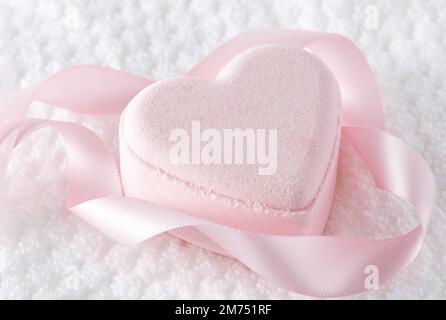 Bomba da bagno rosa tenue circondata da un nastro di seta rosa su un asciugamano bianco; spazio copia Foto Stock