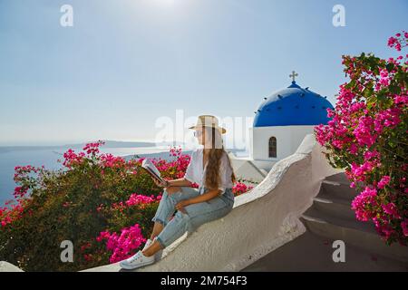 La giovane donna legge un libro seduto sul terrapieno sull'isola di Santorini, Grecia. Foto Stock