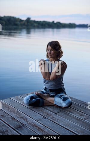 Una donna yoga tranquilla in una posizione loto medita sul molo. Foto Stock