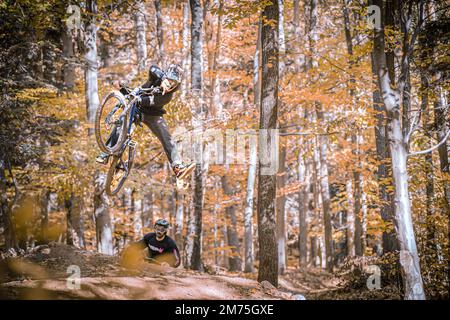 Un'azione orizzontale di due uomini in Holeshotpunx black sportswear distruggendo i sentieri locali in autunno Foto Stock