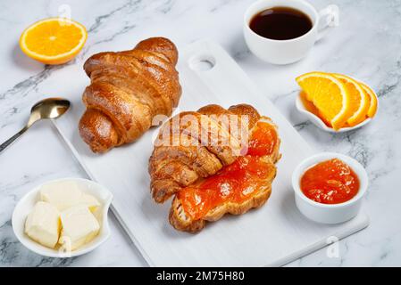 Croissant freschi con burro e marmellata di albicocche per la colazione. Colazione continentale su un tavolo di cemento bianco Foto Stock