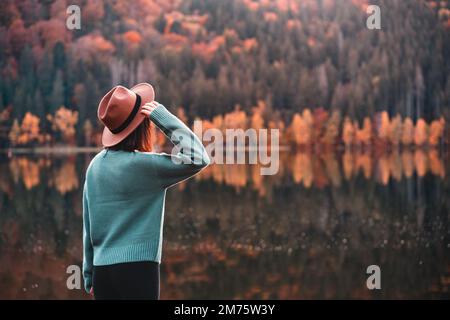 Vista laterale della giovane donna con cappello marrone che guarda la vista sul lago Foto Stock