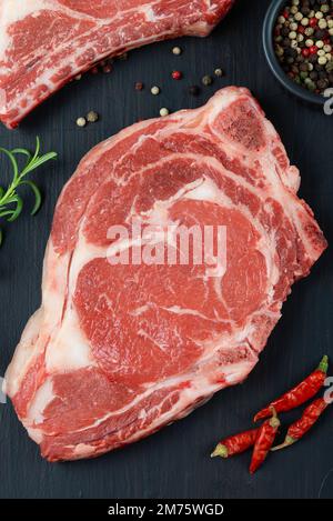 Bistecca di manzo crudo. Black angus prime Meat Set - ribeye, striploin, t-bone bistecche sul tagliere. Vista dall'alto sul tavolo nero Foto Stock