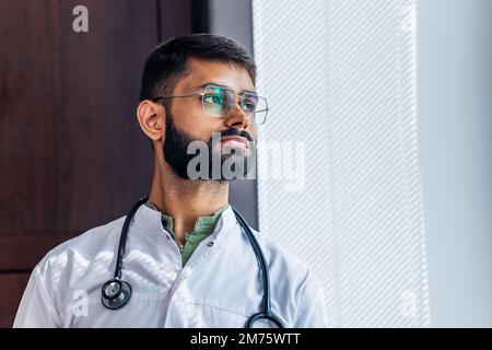 Ritratto di medico indiano maschio che indossa cappotto bianco in clinica ufficio Foto Stock