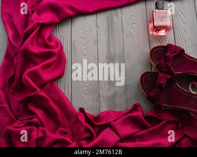 sandali bordeaux zeppa scarpe scialle e bottiglia di profumo rosa. Estate sfondo modello mockup copia spazio libero pattern composizione colorata testo campione Foto Stock