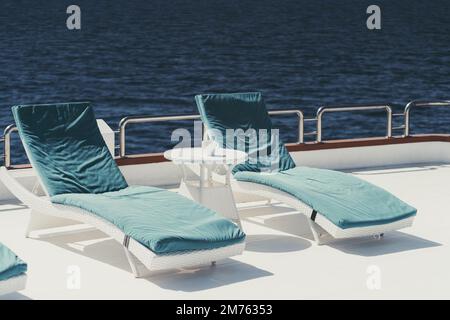 Una foto grandangolare di due poltrone con cuscini blu sulla sommità e un piccolo tavolino di colore bianco sul ponte superiore di una lussuosa barca a vela Foto Stock