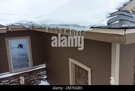 Vista elevata di una diga di ghiaccio e neve su un tetto residenziale. Foto Stock