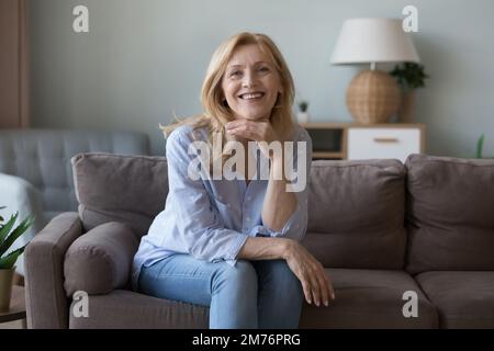 Felice bionda di mezza età attraente donna seduta su comodo divano Foto Stock
