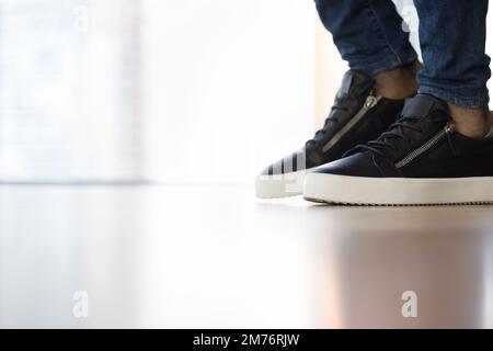 Uomo sconosciuto in sneakers in piedi sul pavimento in interni, primo piano Foto Stock