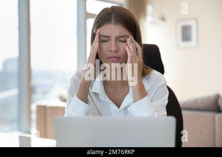 Donna che lavora su un notebook che tocca le tempie, soffre di mal di testa Foto Stock