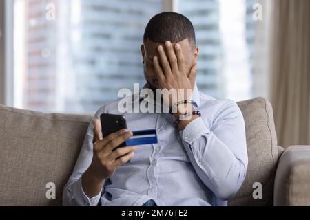 L'uomo tiene la carta e lo smartphone, si sente turbato a causa della truffa Foto Stock
