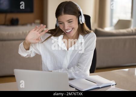 Donna in cuffie rende la videocall, sedersi alla scrivania con il computer portatile Foto Stock