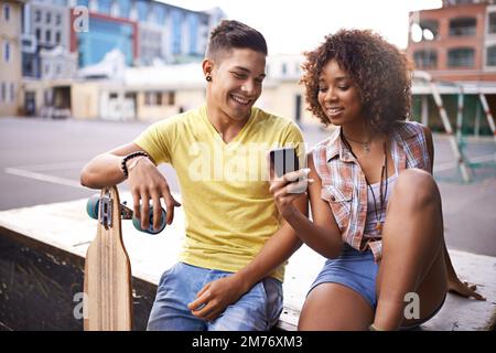 Date un'occhiata a questo. Una giovane coppia che guarda qualcosa su un cellulare mentre fuori skateboard. Foto Stock