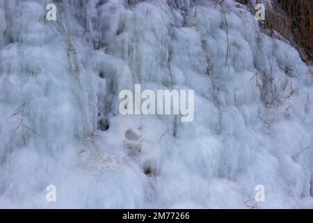 Belle strutture di ghiaccio di una cascata ghiacciata, carine che formano un interessante modello su una roccia scura, creando un'atmosfera fredda e moody dentro Foto Stock