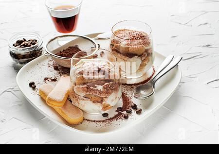 Tiramisù tradizionale dessert italiano in una tazza di vetro. Tiramisù fatto in casa in vasetti di vetro, processo di cottura graduale. Tradizionale dessert italiano non cotto Foto Stock