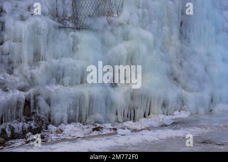 Belle strutture di ghiaccio di una cascata ghiacciata, carine che formano un interessante modello su una roccia scura, creando un'atmosfera fredda e moody dentro Foto Stock