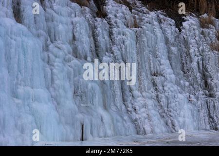 Belle strutture di ghiaccio di una cascata ghiacciata, carine che formano un interessante modello su una roccia scura, creando un'atmosfera fredda e moody dentro Foto Stock