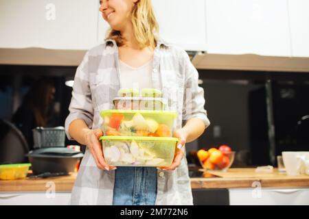 Donna felice tenere contenitori di plastica con diversi alimenti. Conservazione di alimenti ermeticamente sigillata. Cucina a casa. Foto Stock