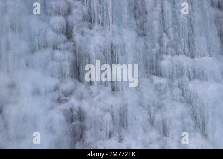 Belle strutture di ghiaccio di una cascata ghiacciata, carine che formano un interessante modello su una roccia scura, creando un'atmosfera fredda e moody dentro Foto Stock