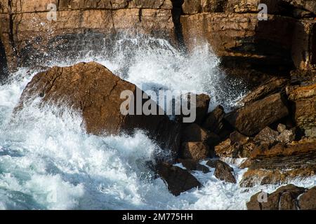 Una potente onda dell'Oceano Atlantico si schianta contro aspre rocce costiere vicino a Guincho Beach, Cascais, Portogallo, durante il sole. Foto Stock