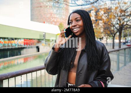 Felice afroamericana donna sorridente e parlando da cellulare all'aperto. Giovane donna che chiacchiera su una conversazione telefonica tramite smartphone. Concetto di comunicazione. Foto di alta qualità Foto Stock