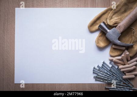 Foglio pulito di acciaio unghie martello a artiglio perni di riferimento in legno e guanti di sicurezza in pelle su tavola di legno concetto di costruzione copyspace. Foto Stock