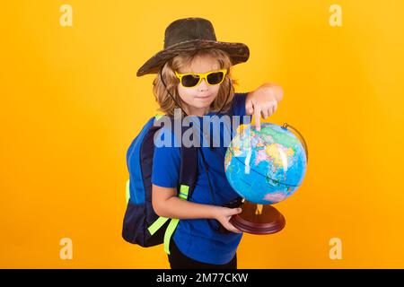 I turisti dei bambini con gli zaini e la macchina fotografica tengono il globo del mondo isolato sullo sfondo giallo dello studio. Bambino con zaini che esplorano il mondo e l'ambiente Foto Stock