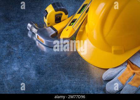 Guanti protettivi casco da costruzione livello nastro-linea e martello a artiglio metallico su sfondo metallico graffiato concetto di manutenzione. Foto Stock