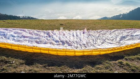 L'uomo su un pendio erboso prepara il parapendio da Vetriolo Terme, provincia di Trento - Trentino Alto Adige - scuola di parapendio - Italia Foto Stock