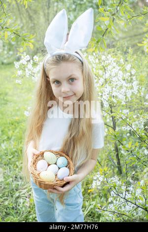 Grazioso fanciullo indossando orecchie di coniglietto il giorno di Pasqua. Ragazza con cesto con uova dipinte. Foto Stock