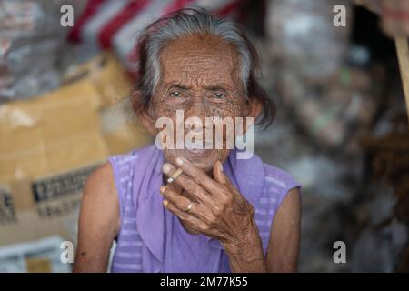 Ritratto di una donna anziana che fuma una sigaretta mentre vende foglie di tabacco in un mercato di strada, Cebu City, Filippine Foto Stock