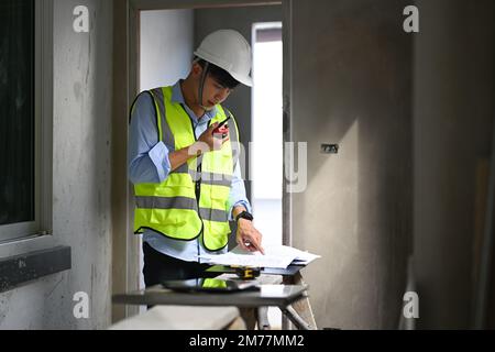 Ingegnere civile che utilizza walkie talkie per comunicare con il team dei colleghi e lavorare con i progetti in cantiere Foto Stock