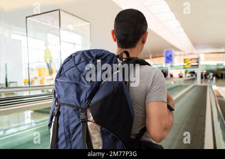 Ripresa da dietro di un giovane uomo irriconoscibile in piedi su una passerella in movimento nell'aeroporto Foto Stock