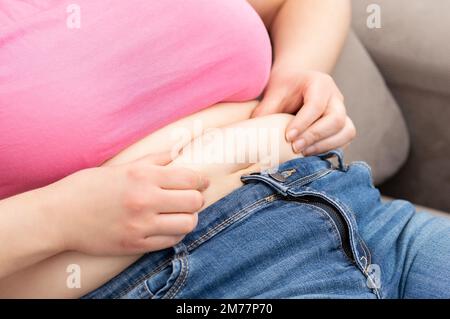 Primo piano di una giovane donna obesa che controlla i suoi grassi seduti su un divano Foto Stock