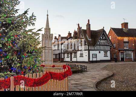 La piazza del mercato acciottolata a Sandbach in Cheshire con il suo albero di Natale e le luci, il monumento commemorativo di guerra cenotafio e la locanda in bianco e nero Foto Stock