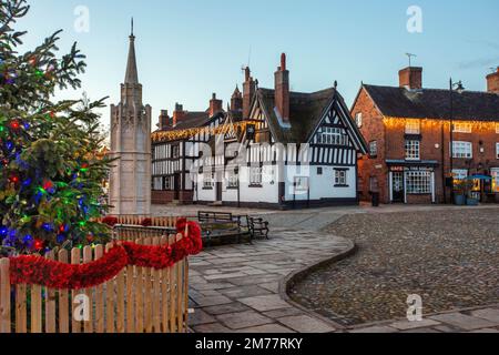 La piazza del mercato acciottolata a Sandbach in Cheshire con il suo albero di Natale e le luci, il monumento commemorativo di guerra cenotafio e la locanda in bianco e nero Foto Stock