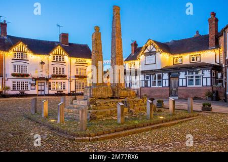 L'antica piazza del mercato acciottolata, illuminata a giorno, nella città del mercato di Cheshire a Sandbach, con le croci sassone e due vecchie locande per le carrozze di notte Foto Stock