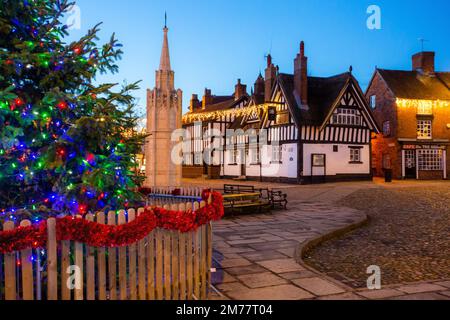 La piazza del mercato acciottolata a Sandbach in Cheshire con il suo albero di Natale e le luci, il monumento commemorativo di guerra cenotafio e la locanda in bianco e nero Foto Stock