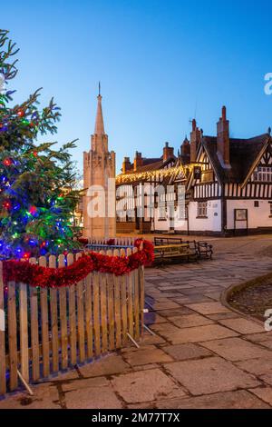 La piazza del mercato acciottolata a Sandbach in Cheshire con il suo albero di Natale e le luci, il monumento commemorativo di guerra cenotafio e la locanda in bianco e nero Foto Stock