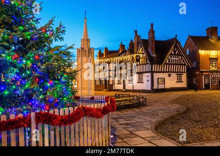 La piazza del mercato acciottolata a Sandbach in Cheshire con il suo albero di Natale e le luci, il monumento commemorativo di guerra cenotafio e la locanda in bianco e nero Foto Stock