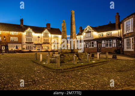 L'antica piazza del mercato acciottolata, illuminata a giorno, nella città del mercato di Cheshire a Sandbach, con le croci sassone e due vecchie locande per le carrozze di notte Foto Stock