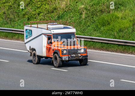 2006 Classic Orange LAND ROVER DEFENDER 130 TD5 trasformato in motorhome, con verricello, plafoniera e pannello solare; viaggiando sull'autostrada M6 UK Foto Stock