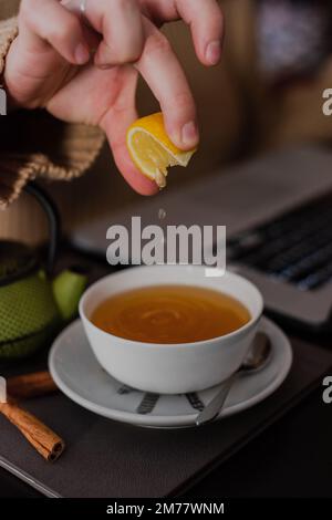 Un primo piano di una ragazza che strizza il limone in una tazza di tè in un bar con bastoncini di cannella accanto ad esso Foto Stock