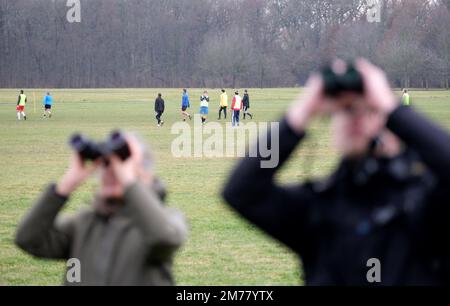 Lipsia, Germania. 08th Jan, 2023. I partecipanti a un conteggio di uccelli guardano attraverso binocoli in un parco mentre i giocatori di calcio dilettanti si esercitano in background. Gli osservatori di uccelli si riuniscono per il "conte di uccelli invernali" organizzato dall'Unione tedesca per la conservazione della natura e della biodiversità (NABU). La campagna partecipativa a livello nazionale invita le persone interessate a trascorrere un'ora a contare gli uccelli nelle aree urbane e a segnalarli a Nabu. Credit: Sebastian Willnow/dpa/Alamy Live News Foto Stock