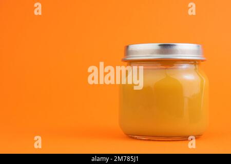 Purea di frutta o verdura in scatola in un vasetto di vetro su sfondo arancione. Il concetto di alimenti per bambini, alimenti in scatola, ortaggi o frutta. Spazio di copia Foto Stock