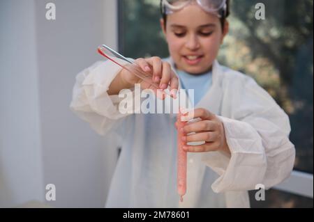 Primo piano le mani dello scolaro tengono le provette con la soluzione che fuoriesce, la reazione chimica si verifica durante una lezione di chimica Foto Stock